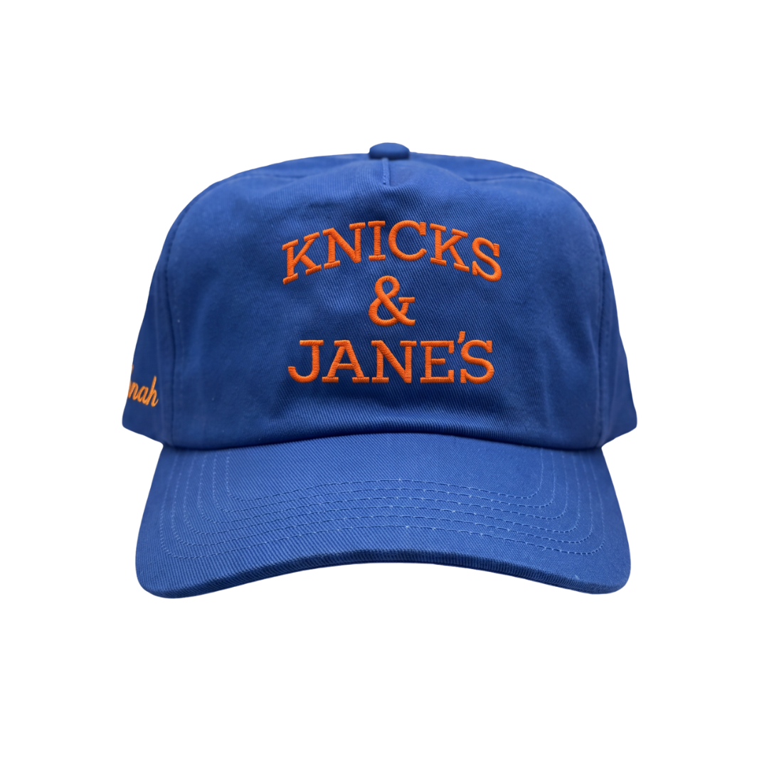 A royal blue baseball cap with orange embroidered text reading 'KNICKS & JANE'S' on the front, shown against a plain white background.